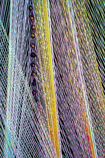 A diversity of colors of cotton string are interwoven.  Rows upon rows of intertwined thread form a diagonal repeating pattern.  There are nails grounding the thread. String art