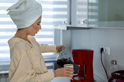 A beautiful young woman is preparing a cup of espresso coffee early in the morning.