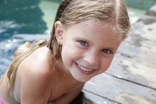Portrait of adorable cheerful 5 years old girl with wet hair in swimming pool