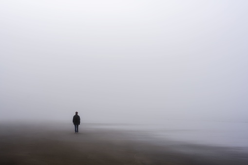 A solitary woman figure walking along a fog-shrouded beach