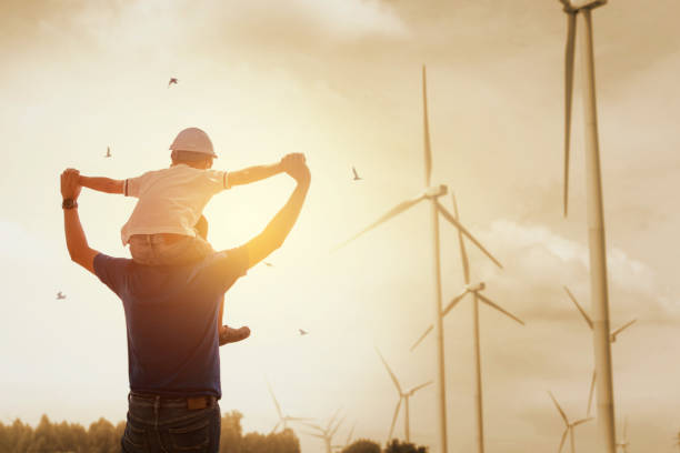 Happy dad carrying son on shoulders checking future project at wind farm site on sunset. Silhouette of father and son. stock photo