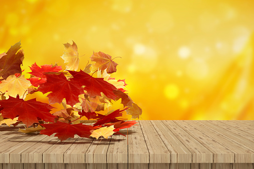 Autumn leaves flying over wooden desk, bokeh background, digitally generated image.