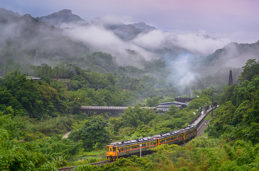 A yellow diesel train is driving in the mountains and forests. Along the Pingxi line, there are river valleys, potholes and waterfalls. Taiwan