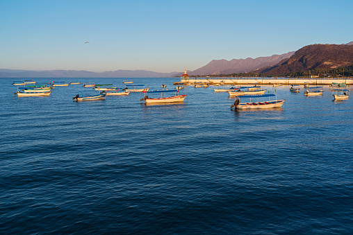 Chapala, JALISCO/MEXICO - March 4, 2023: Boats anchored and pier on Lake Chapala with mountains along horizon at daybreak.