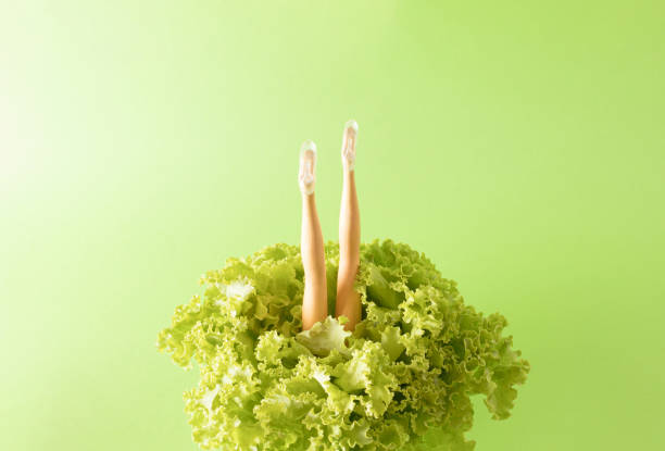 Minimal composition with doll legs in lettuce with bright green background. Creative healthy food and life concept. Close up.