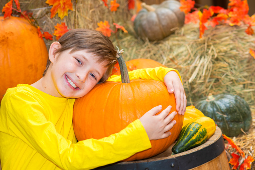 happy boy sits on the hay and hugs the pumpkin at the farm. joyful child celebrates thanksgiving day.