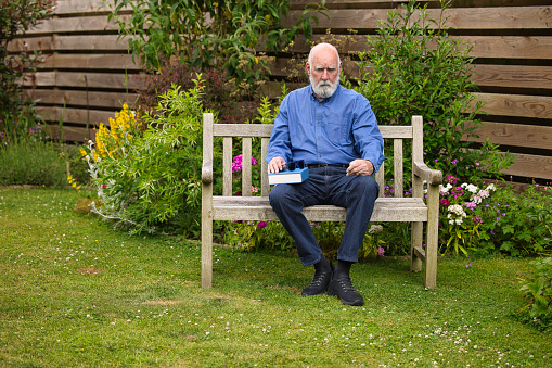 Casually-dressed man in his 70s sitting out in his garden.