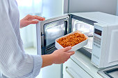 Female warming up a container of food in the modern microwave oven for snack lunch at home