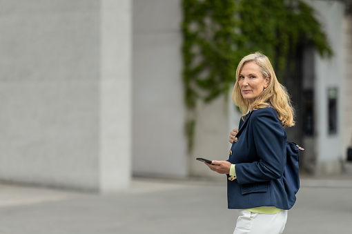 A business woman, casually dressed, walks through the streets of the city, in a good mood, smiling, talking on the phone and enjoying a sunny day.
Copy space, portrait.