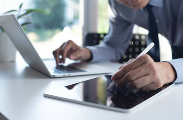 istock Businessman using digital tablet and working on laptop computer on office table. Corportae man using stylus pen proofing and signing e-document on tablet pc 1499453156