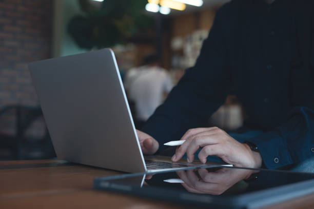 istock Man working on laptop computer and using digital tablet surfing the internet on wooden table at coffee shop 1499453164