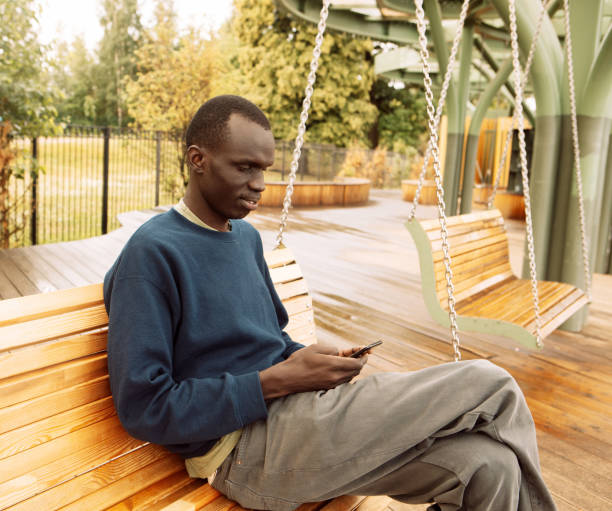 istock Young african american sitting on a tree in park with mobile phone 1499456599