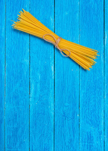 Package of spaghetti tied with natural jute twine and two open cans on vintage weathered blue wooden boards. Vertical photo