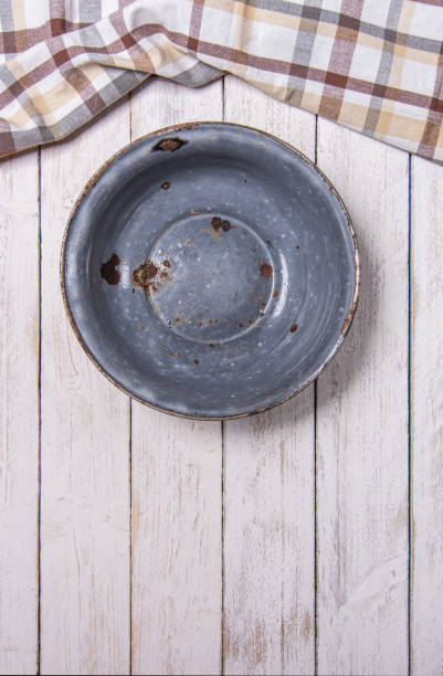 istock Old vintage enameled rusty bowl on white wooden desk and checkered kitchen cloth on top side. Vertical photo. 1499457421