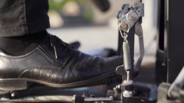 Close-up of man drummer leg in black shoes hitting bass drum with pedal