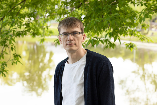 Portrait Of Tall Fit Blond 40 Yo Male In Eyesight Glasses, Smiling Looking At Camera, Green Tree And Lake On Background. Horizontal Plane. High quality photo