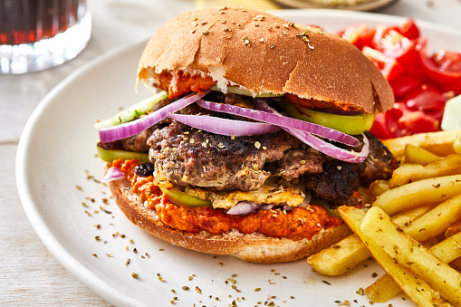 Fresh, tasty and delicious beef hamburger with French fries, tomato and pepper red salsa, Spanish onion, garlic, egg and green pepper, served  on a plate, bar, restaurant or home kitchen table, close up view with copy space, representing fast food and city life, indulgence and joy through gourmet lifestyle