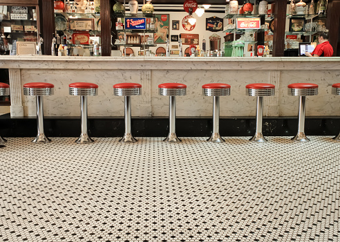 Red stools at a marble bar in a historic diner with a black and white tiled floor