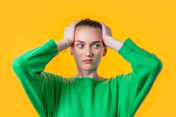 istock Woman afraid of something, she in shock on yellow backdrop.Holding head 1499472859