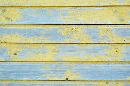 The wall of a wooden barn with peeling yellow paint. Bright background of old paint on the boards