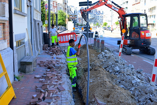 Blankenberge, West-Flanders, Belgium- June 12, 2023: Turkish road workers are opening up the street and laying pipelines of telecom infrastructure such as fiber optics