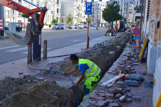 Fiber optics road construction Blankenberge Blankenberge, West-Flanders, Belgium- June 12, 2023: Turkish road workers are opening up the street and laying pipelines of telecom infrastructure such as fiber optics laying underground pipes stock pictures, royalty-free photos & images