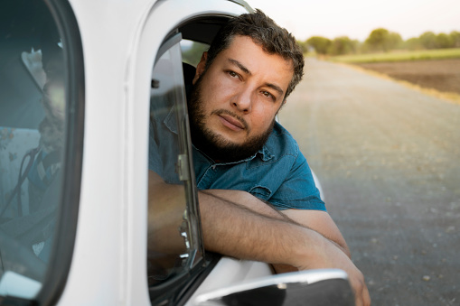 close up portrait of young man leaning out the window of his classic car while traveling on the road