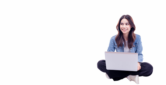 Young woman sitting on floor legs crossed using laptop computer on white background Smiling student teenager girl working on laptop computer Full body young girl work on netbook looking to empty space