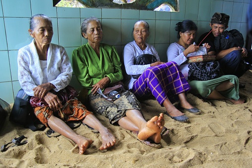 Yogyakarta, Indonesia, March 5, 2015. Elderly Hindu devotees sit on the sand solemnly attending the Melasti religious event.