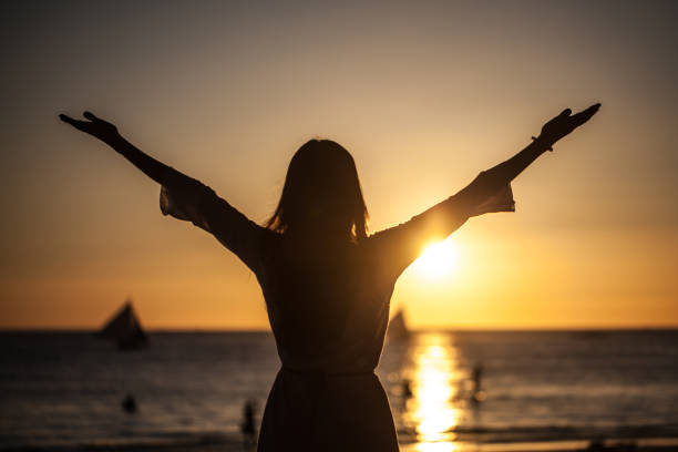 Woman raising arms to sunset stock photo