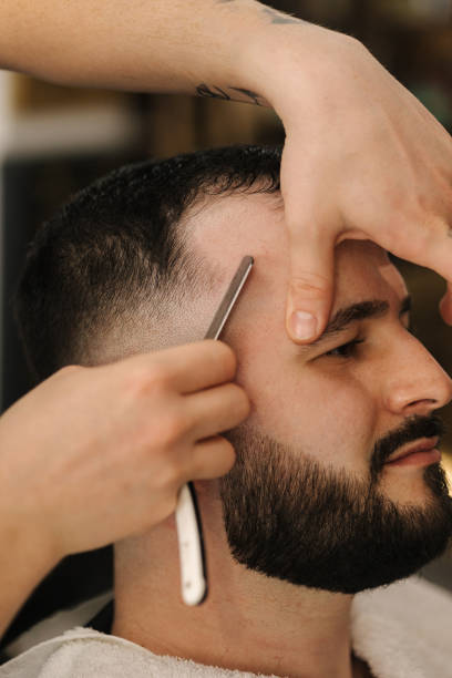 istock Side view of barber using sharp blade for shaving. Handsome customer sitting in barbershop 1499495404