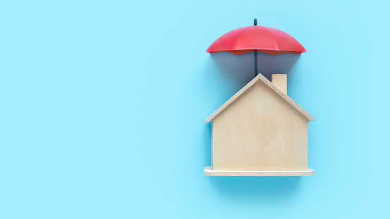 Concept of property insurance, mortgage, real estate. Umbrella over a wooden house model.