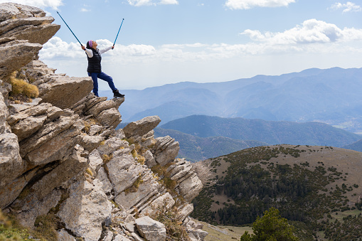Latin woman from a rock at the top of the mountain raises her sticks for the wonderful landscape that has allowed her to climb and trekking days