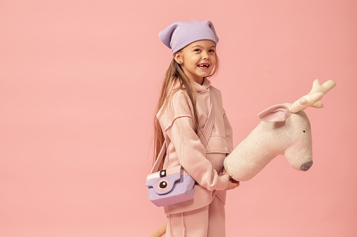 Portrait of sleeping and smiling five-year-old red-haired kid girl with closed eyes in orange sweatshirt, holding small redhair doll in hands at her face over white background with copy space