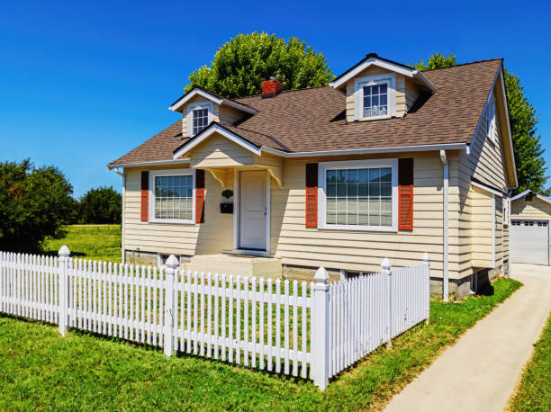 Small Yellow Suburban House Exterior with White Picket Fence Photo of a small yellow suburban home with a white picket fence surrounding the front yard, on a sunny summer day picket fence stock pictures, royalty-free photos & images