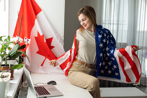 Picture of happy young lady with USA flag using laptop computer. Looking camera. High quality photo