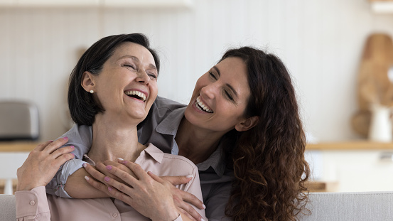 Cheerful daughter woman hugging happy excited mature mom with love, gratitude, joy, celebrating mothers day, laughing out loud, having fun. Mother and adult kid casual home portrait