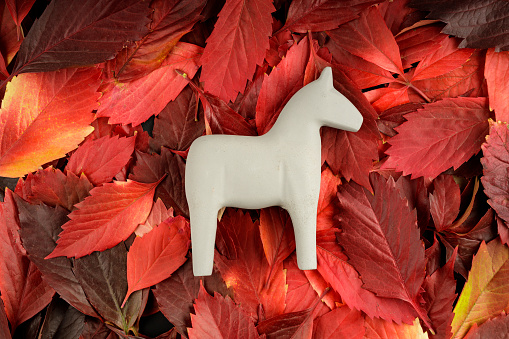 a gray toy horse is located on a surface of red autumn leaves. autumn gray melancholy in the form of a horse