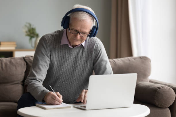 istock Focused senior retired man in wireless earphones writing in copybook 1499524959