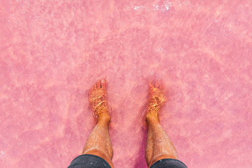 Young mans feet standing in a bright pink salt lake in the South Australian outback.