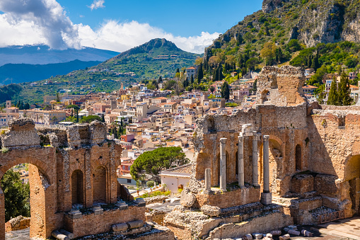 Taormina on Sicily, Italy. Ruins of ancient Greek theater, mount Etna covered with clouds. Taormina old town and mountain in background. Popular touristic destination on Sicily.