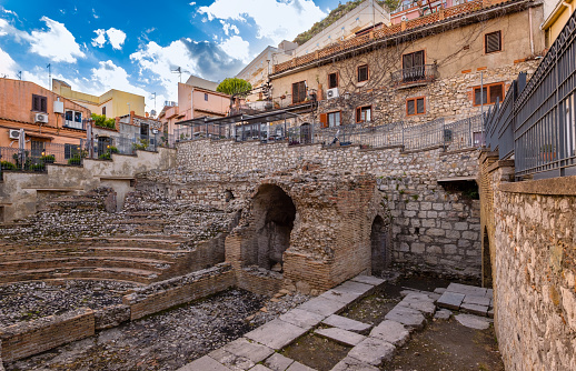 Odeon in Taormina, Sicily island in Italy. Ruins of ancient greek theater in old town, antique amphitheater among among modern buildings. Famous tourist attraction.