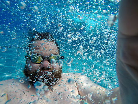 Man dives under water.  In a swimming pool with blue water and air bubbles
