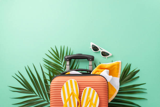 istock Let your imagination take flight against a turquoise backdrop, showcasing top view of a suitcase with towel, beach gear, sunglasses, flip-flops and palm leaves. Ideal for travel branding 1499543547
