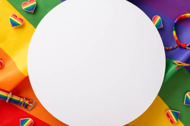 istock Vibrant LGBTQ parade accessories in a top view flat lay, featuring a multicolored bracelet, wristlet, heart shaped pin badges on a rainbow flag background with an empty circle perfect for text or ads 1499545112