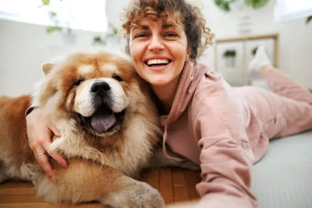 Young beautiful woman taking selfie with her chow chow dog at apartment, she is laying down on exercise mat