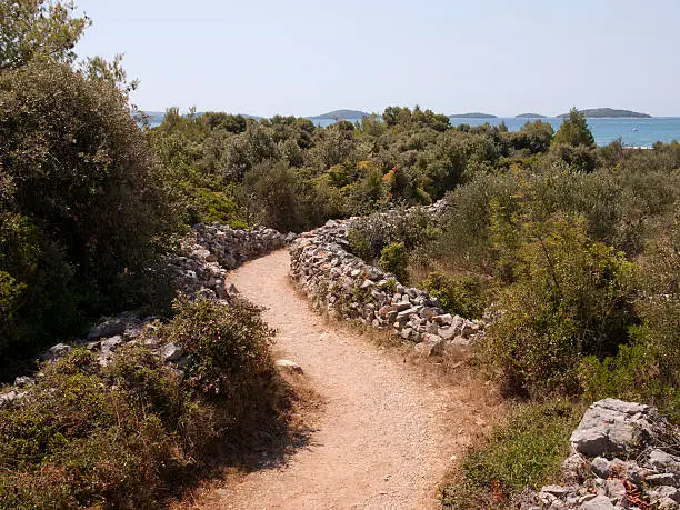 Dry wall-bordered path down to a beach at adriatic sea in Solaris, Croatia with some islands in the distant horizon.