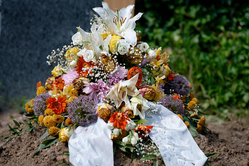 colorful flower arrangement with white bow on a freshly filled grave after a funeral