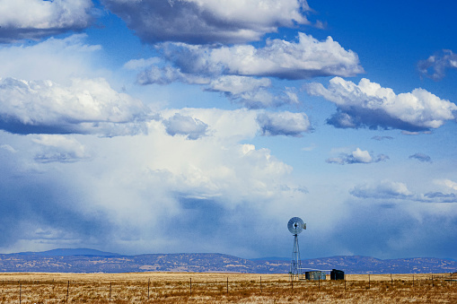 Landscape of farmland, with old Windmill and Cloudy Sky in Background.\n\nTaken in Central California, USA