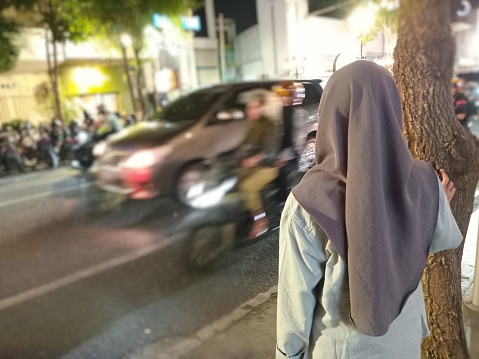 Small hijab girl  who will cross in a busy street of vehicles in Surabaya, Indonesia.
